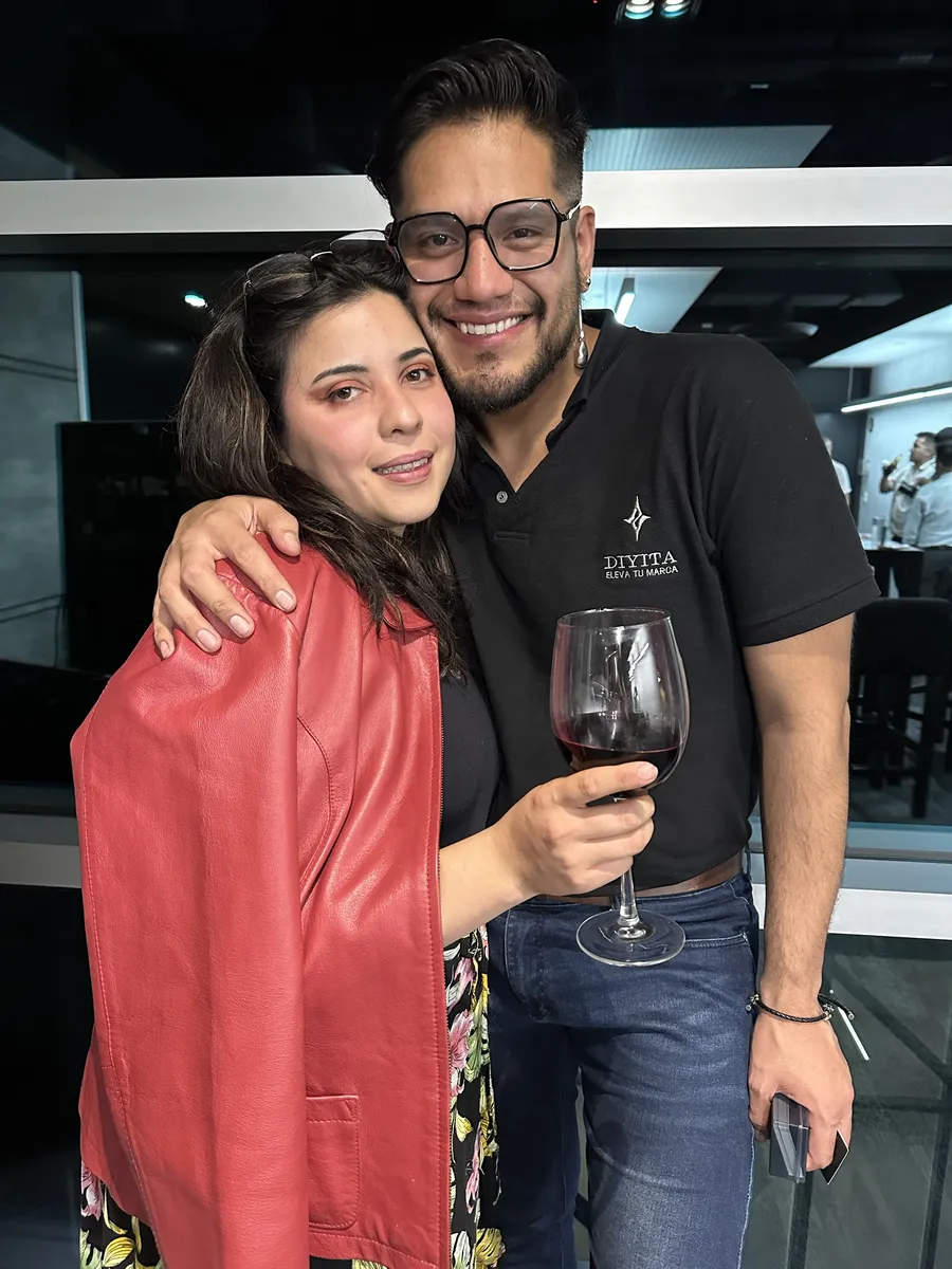 Dos asistentes abrazados con una copa de vino